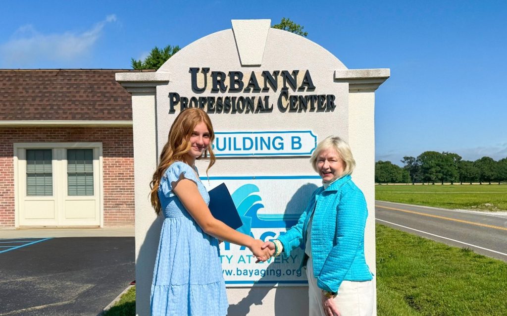 Two women Shaking hands in front of sign