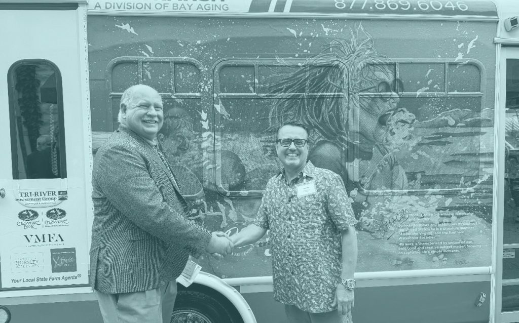 Two men shaking hands in front of bus with mural