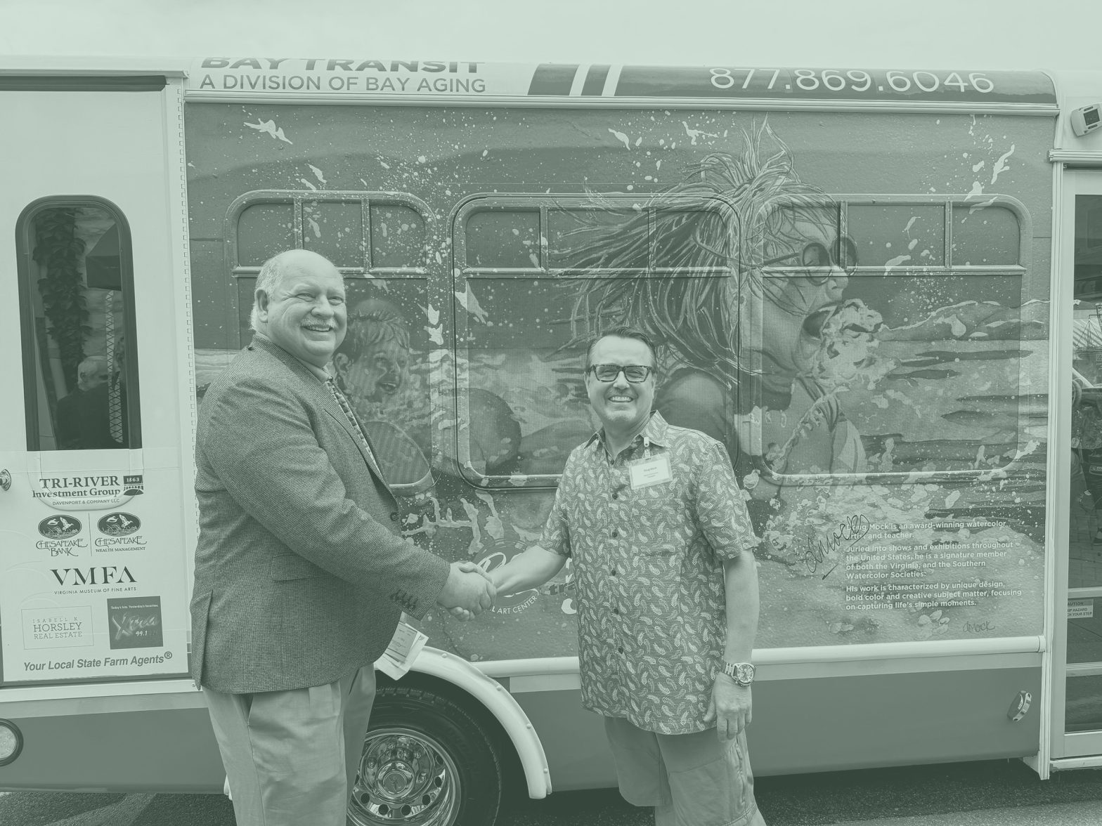 Two men shaking hands in front of bus with artwork